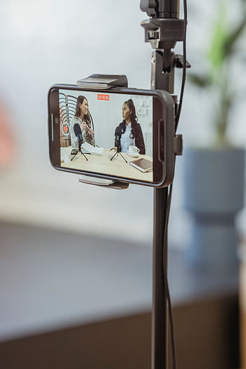Two women podcasters engage in a conversation while recording on a smart setup in a studio. HD phone wallpaper