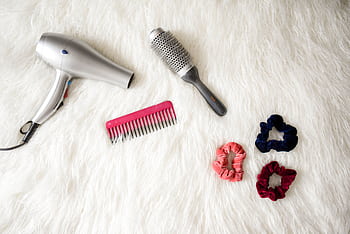 Flatlay of hairstyling tools including a hairdryer, brush, comb, and scrunchies on white fur. HD wallpaper