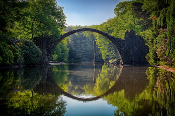 Capture of the iconic Rakotzbrücke reflecting in calm waters amidst lush greenery in Germany. HD wallpaper