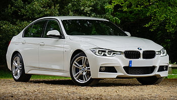 White BMW car parked on gravel path surrounded by greenery, showcasing luxury design. HD wallpaper