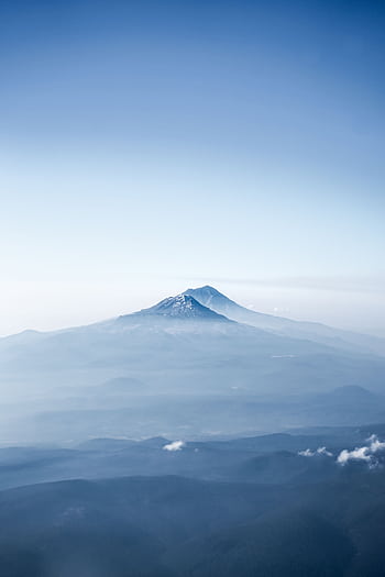 A breathtaking aerial shot of a snow-capped mountain peak surrounded by fog and clouds, capturing the serene beauty of nature. HD phone wallpaper