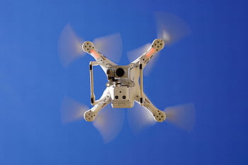 Aerial view of white drone flying with rotating blades against a clear blue sky, capturing video footage. HD wallpaper
