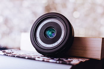 Detailed close-up of a Canon camera lens resting on books, surrounded by a soft bokeh backdrop. HD wallpaper