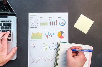 Hands interacting with charts and notes for data analysis on a desk. HD wallpaper