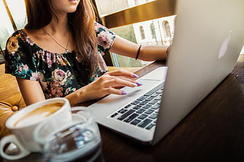 A woman working on a laptop in a cafe, sipping coffee, embodying a modern remote work lifestyle. HD wallpaper