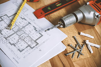 Close-up of construction blueprint with tools like drill and screws on a wooden table. HD wallpaper