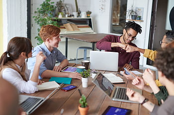 A diverse group of young professionals brainstorming around a table in a modern office environment. HD wallpaper