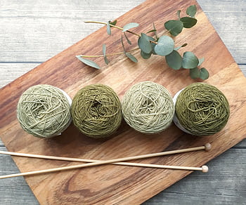 A flat lay of green yarn balls and knitting needles on wood, evoking creativity and craftsmanship. HD wallpaper