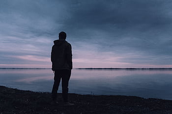 A solitary silhouette of a man in a jacket gazing at a lake during a peaceful sunset, creating a serene atmosphere. HD wallpaper