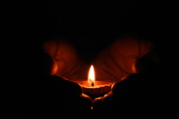 Close-up of hands warmly embracing a lit candle in the dark, creating a cozy atmosphere. HD wallpaper