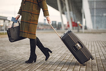 A fashionable woman in a coat walks with luggage and a handbag outdoors. Ideal travel concept. HD wallpaper