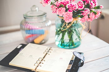 A chic desk setup with an open planner and a vase of pink flowers, ideal for productivity. HD wallpaper