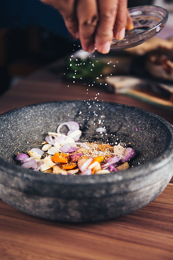 Close-up of seasoning being added to fresh ingredients in a stone bowl, perfect for culinary themes. HD phone wallpaper