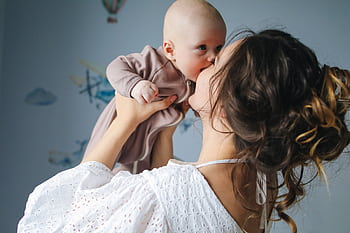 A heartwarming scene of a mother lovingly kissing her baby in a decorated room. HD wallpaper