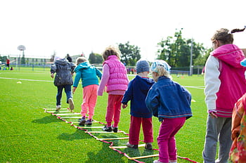 Children enjoy an outdoor activity on a grassy field, stepping over a ladder. HD wallpaper
