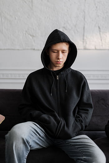 Teenager in a black hoodie sitting on a couch, reflecting on thoughts indoors. HD phone wallpaper
