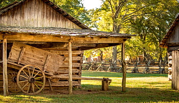 A rustic wooden barn with an old wooden wagon in a sunny outdoor farm setting. HD wallpaper