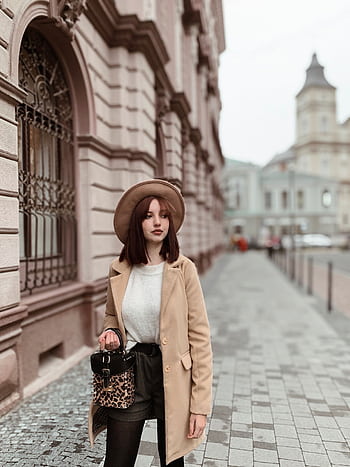 Fashionable woman wearing a hat and coat strolling through a city street with classic architecture. HD phone wallpaper