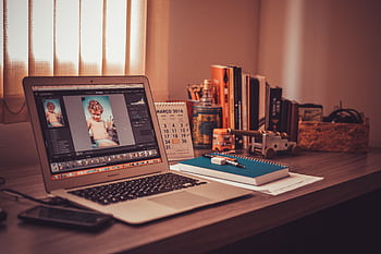 Warm-toned home office desk with a laptop, notebook, and books. Perfect for lancers. HD wallpaper