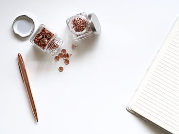 A minimalist flat lay of office supplies including a notebook, pen, and jars of clips on a white background. HD wallpaper