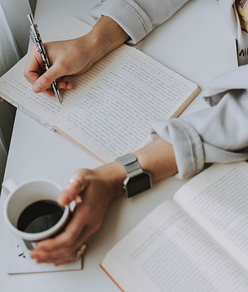 Close-up of a person writing in a notebook with coffee on a desk. Ideal for workplace or study themes. HD phone wallpaper