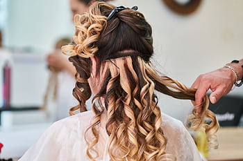 Close-up of hairstylist perfecting curls on a woman's hair in a salon setting. HD wallpaper