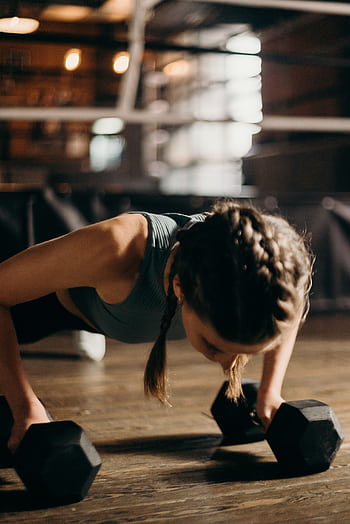 Fit woman doing push-ups with dumbbells indoors, emphasizing strength training and fitness. HD phone wallpaper