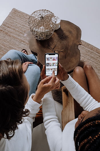 Two people looking at social media on a smart at a wooden table. HD phone wallpaper