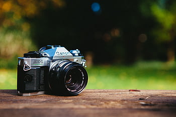 Close-up of a classic vintage analog camera on a wooden table outdoors, with a blurred green background. HD wallpaper