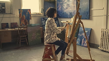 A young woman focused on painting in an art studio filled with her work. HD wallpaper