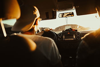 Man driving car with passenger at sunset, capturing warm sunlit atmosphere. HD wallpaper