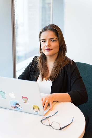 Confident businesswoman using laptop for remote work in a stylish office setting. HD phone wallpaper