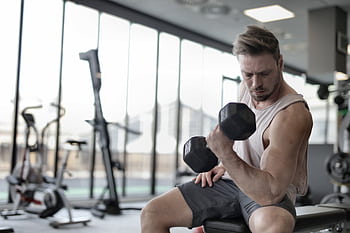 Focused man working out with a dumbbell in a well-equipped gym for strength training. HD wallpaper