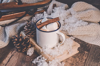 A cozy winter scene with hot chocolate, cinnamon, and marshmallows by a rustic sled and pine cones. HD wallpaper