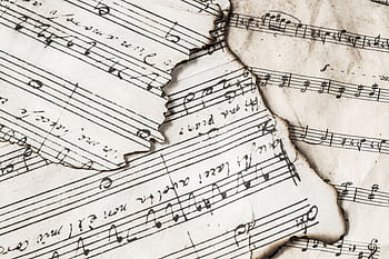 Close-up of aged, burnt music sheets displaying musical notes and compositions in detail. HD wallpaper