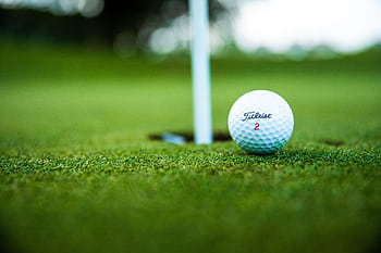 A close-up shot of a Titleist golf ball close to the hole on a green golf course. HD wallpaper