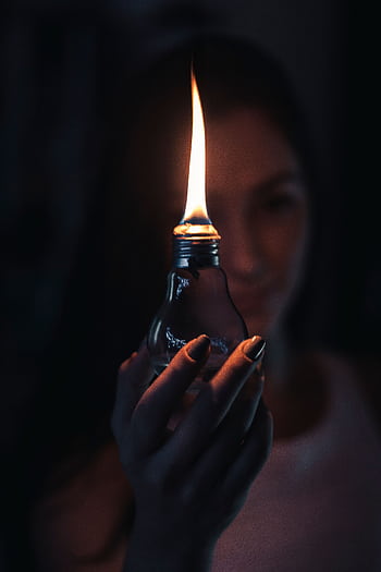 A glowing flame inside a light bulb held by a woman, creating a warm and mysterious ambiance. HD phone wallpaper