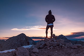 Person standing on a rocky mountain peak at sunset in Tolmin, Slovenia, embracing nature's beauty. HD wallpaper