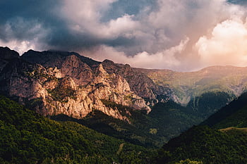 Stunning view of a mountain range under dramatic clouds and vibrant lighting. HD wallpaper