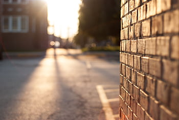 Close-up of a sunlit brick wall with blurred urban street in the background at sunset. HD wallpaper
