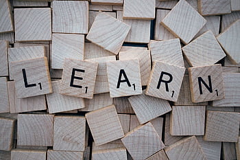 Wooden letter tiles arranged to spell 'learn' on a background of scattered tiles. HD wallpaper