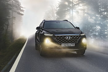Black SUV driving on a misty forest road with headlights on, creating a dramatic scene. HD wallpaper