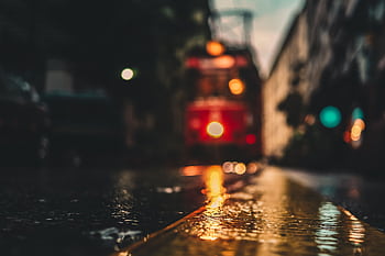 A moody, blurry shot of an urban street reflecting lights with a tram in the background. HD wallpaper