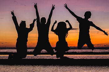 Silhouette of friends jumping on the beach at sunset, celebrating summer fun. HD wallpaper