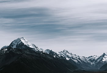 Breathtaking view of snow-capped mountain peaks under a cloudy sky. HD wallpaper