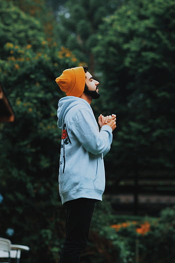 A man in a beanie and hoodie deeply praying outside in a lush green forest. HD phone wallpaper