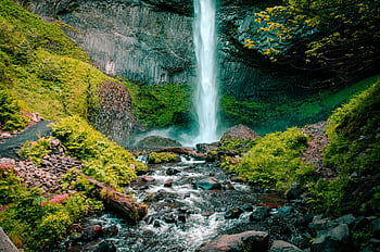 Majestic waterfall cascading down rocky cliff surrounded by vibrant greenery in a serene outdoor location. HD wallpaper