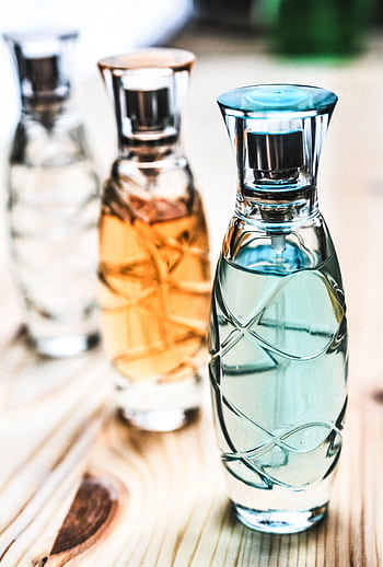 Artistic shot of elegant perfume bottles with colorful liquids on a wooden surface. HD phone wallpaper