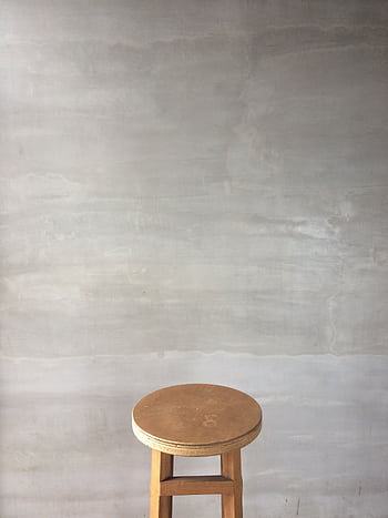 A minimalist wooden stool placed against a light grey wall, ideal for interior design concepts. HD phone wallpaper
