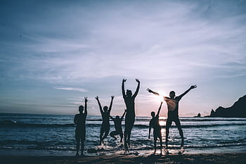 Silhouetted group of friends jumping joyfully on the beach at sunset, symbolizing dom and happiness. HD wallpaper